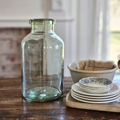 a glass bottle sitting on top of a wooden table next to plates and bowls in front of it