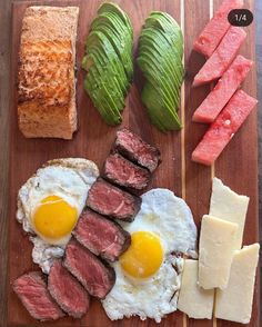 an assortment of food on a cutting board including meat, eggs and bread with sliced watermelon