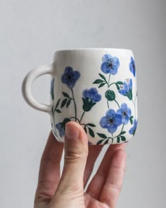 a hand holding a coffee cup with blue flowers on it