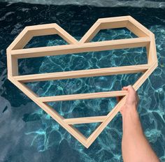 a person holding up a wooden heart shaped object in the water with their right hand