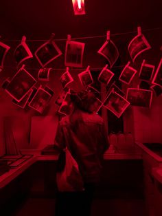 a person standing in a room with pictures hanging from the ceiling and red light shining on them