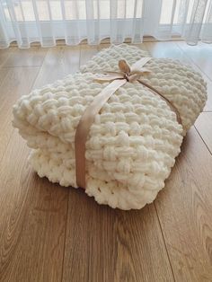 a pile of white knitted blankets with a ribbon tied around the edges on a wooden floor