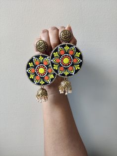 a woman's hand holding two colorful earrings on top of each other with bells hanging from them