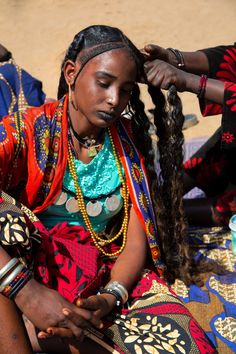 a woman is sitting on the ground with her hair in braids and wearing jewelry