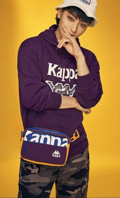 a young man in a purple sweatshirt and camo pants poses with his hand on his chin