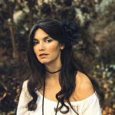 a woman with long hair wearing a white shirt and black flower in her hair is standing outside