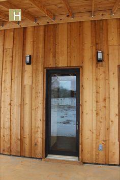 a wooden building with a black door and two lights on the side of it's wall