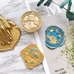 three different gold and blue coins sitting on top of a marble table next to a plant