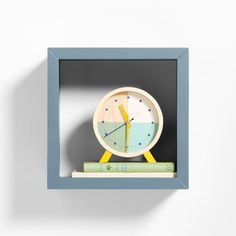 a small clock sitting on top of a book shelf next to a wall mounted frame