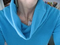 a woman wearing a blue sweater with a silver necklace on it's neck is looking at the camera