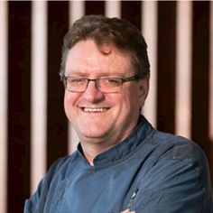 a man with glasses and a blue shirt is smiling at the camera while he has his arms crossed in front of him