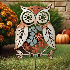 an owl statue sitting on top of a metal stand next to flowers and pumpkins