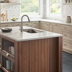 a kitchen with white cabinets and marble counter tops is pictured in this image, there are two windows above the sink