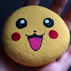 a hand holding a yellow and red painted rock with a smiley face on it's side