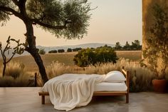 a bed sitting next to a tree on top of a cement floor covered in white blankets