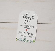 a thank you tag on a white wooden background with greenery and hearts in the center