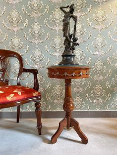 a chair and table in front of a wallpapered wall with a statue on it