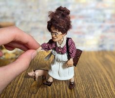 a small doll is being held by a person's hand on a wooden table