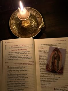 an open book with a lit candle on top of it next to a metal plate