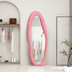 there is a pink mirror on the wall next to a shelf with shoes and purses