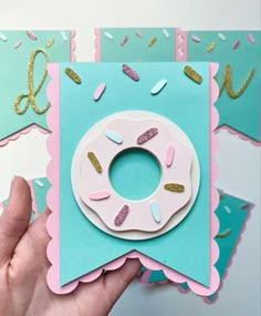 a hand holding up a pink and blue card with a doughnut on it, surrounded by confetti