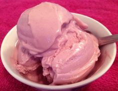 two scoops of ice cream in a white bowl on a pink towel with a wooden spoon