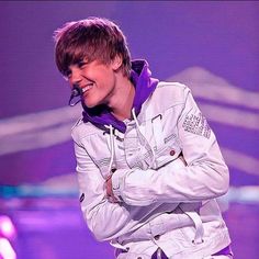 a male in a white jacket and purple hoodie is smiling at the camera with his arms crossed