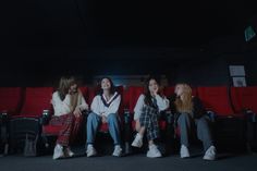 four young women sitting on red seats in an empty room with their backs turned to the side