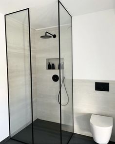 a bathroom with a glass shower stall and black flooring, along with a white toilet