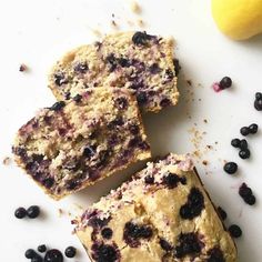 three blueberry muffins sitting on top of a white surface next to a lemon