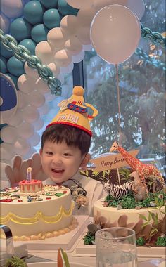 a young boy wearing a birthday hat sitting in front of a cake