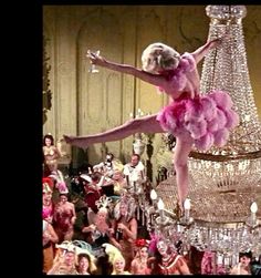 a woman in pink is dancing on a chandelier with lots of people watching