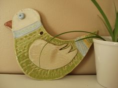 a ceramic bird sitting next to a potted plant on a shelf with a wall in the background