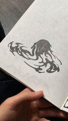 a person is holding an open book with drawings on it and the pages are covered in black ink