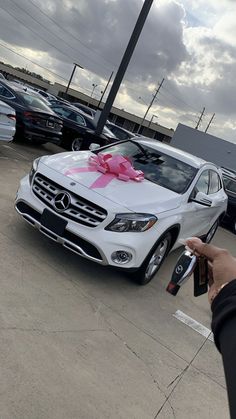 a person holding a remote control in front of a car with a pink bow on it