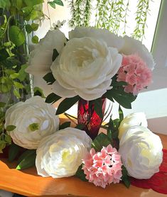 a vase filled with white and pink flowers on top of a wooden table next to a window