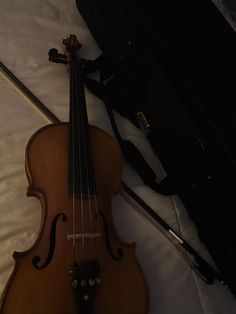 an old violin laying on top of a bed next to a black case and bow