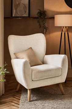 a white chair sitting on top of a wooden floor next to a lamp and window