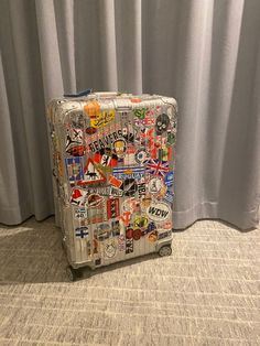 a piece of luggage with stickers all over it sitting on the floor next to a curtain