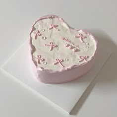 a cake shaped like a heart on top of a white card with pink ribbon and bows