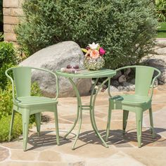 two green chairs and a small table in front of some rocks with flowers on it