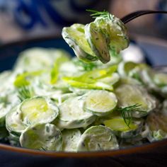 cucumber salad in a bowl being spooned with a black fork and topped with dill