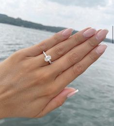 a woman's hand holding an engagement ring on the edge of a body of water