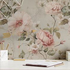 a desk with a notebook and pen on it next to a flower wallpaper mural