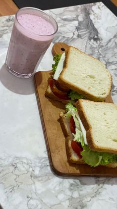 two sandwiches on a cutting board next to a glass of milk and strawberry smoothie