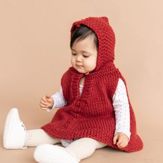 a small child wearing a red knitted vest and white leggings sitting on the floor