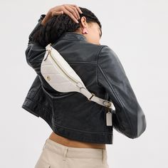 a woman wearing a black leather jacket with a white fanny bag on her back and shoulder