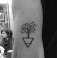 a black and white photo of a tree tattoo on the left inner arm, with people in the background