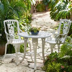 two white chairs and a table in the middle of a garden with potted plants