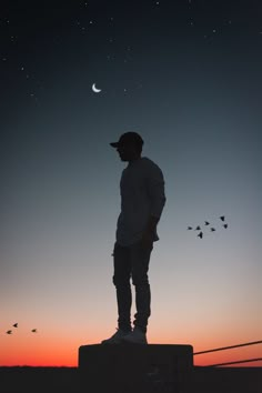 a man standing on top of a cement block under a sky filled with stars and birds